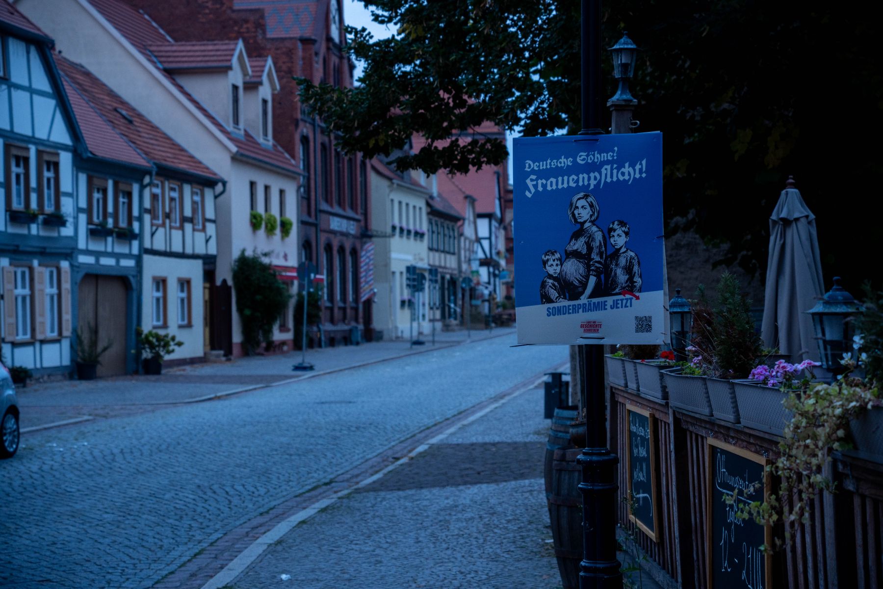 Plakat „Deutsche Söhne? Frauenpflicht! Sonderprämie jetzt“ an einer Laterne unterhalb der Burg
